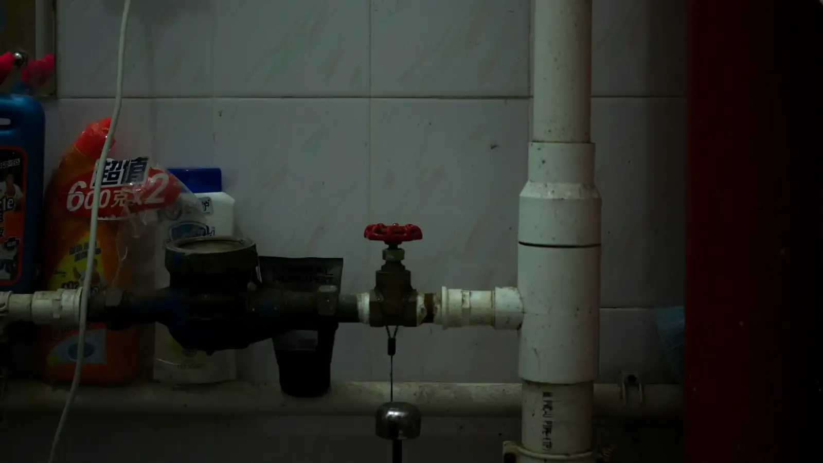 A red shutoff valve on a vertical white drain pipe beside a water meter